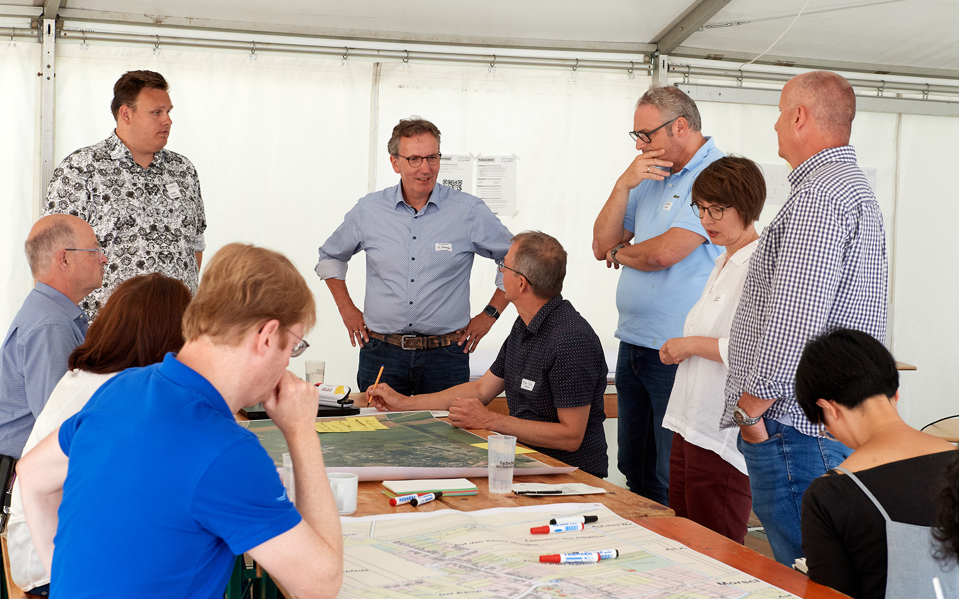 Zu sehen ist eine Gruppe von Menschen, die miteinander diskutieren und Notizen auf einem Luftbild vermerken.