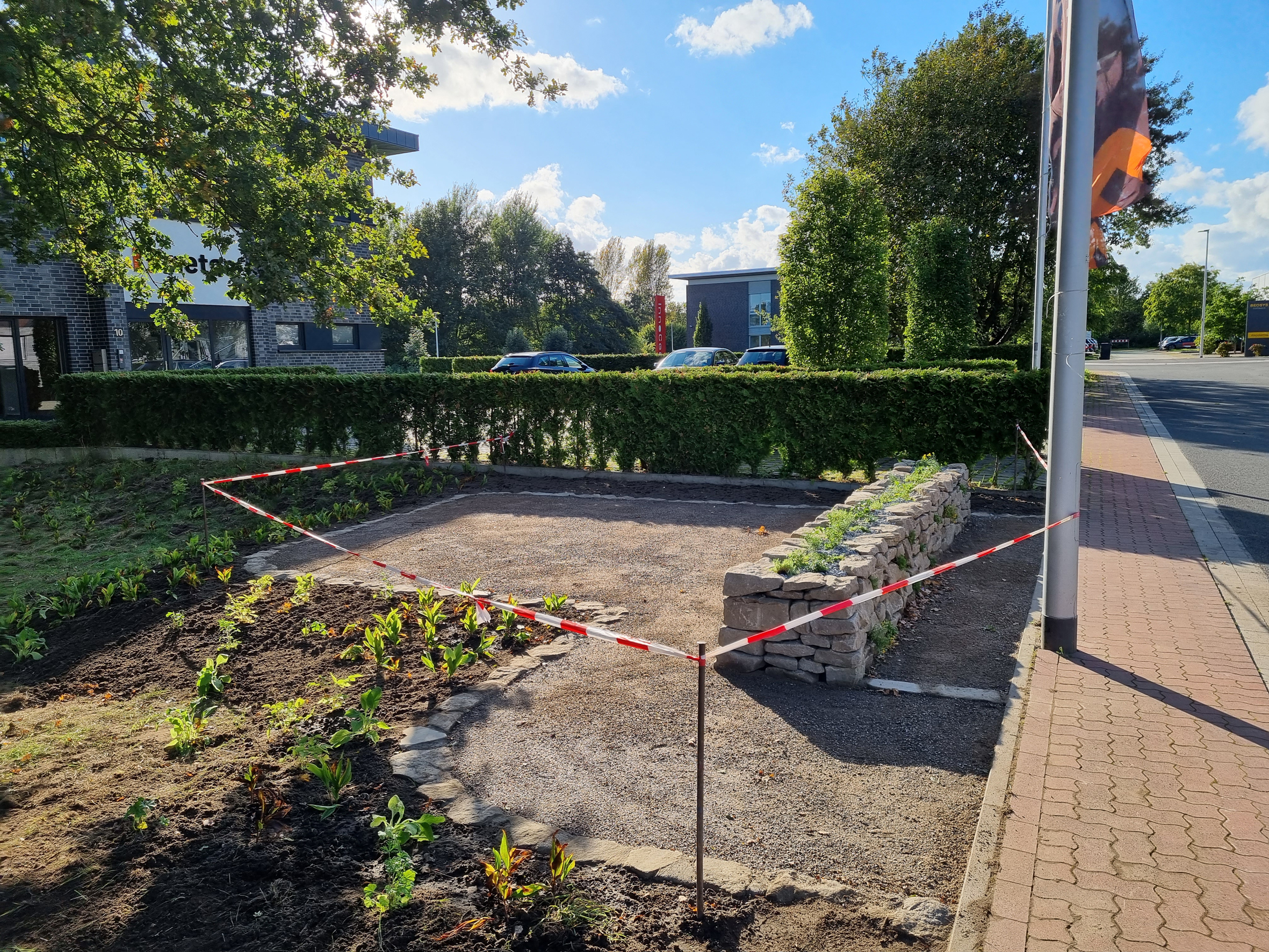 Eine frisch angelegte Pflanzung mit Natursteinmauer und einer wassergebundenen Platzfläche.